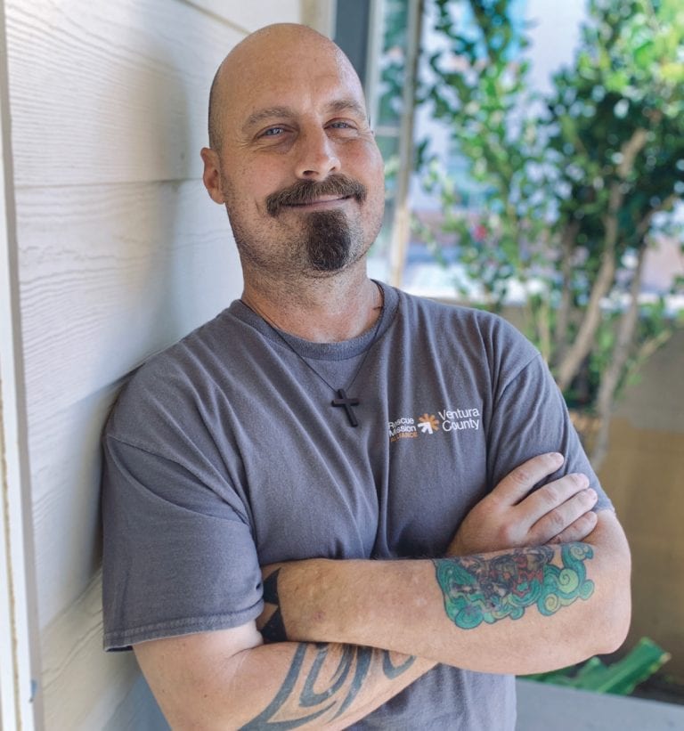 Man with tattoos smiling outdoors at San Fernando Rescue Mission.