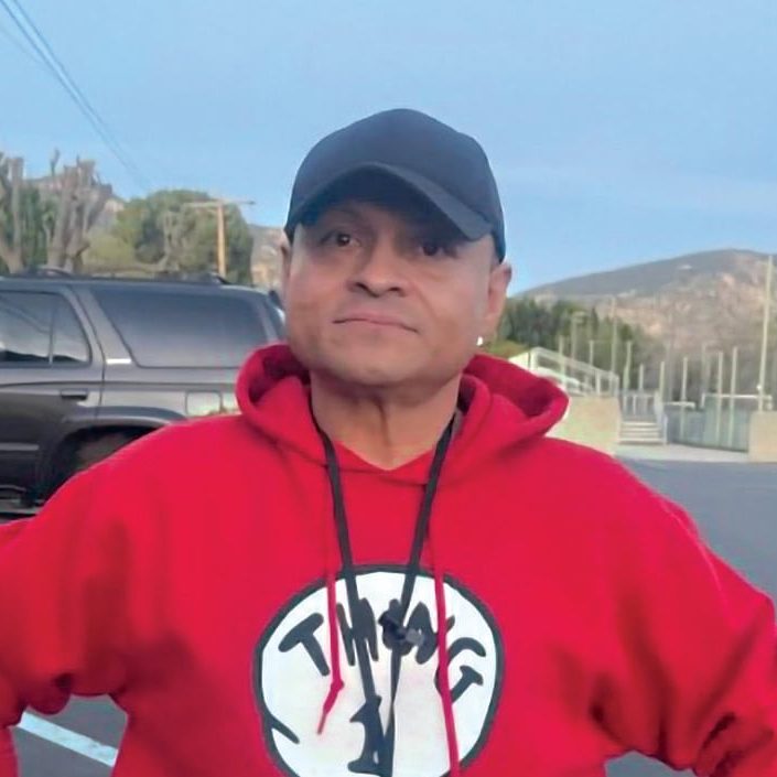 A man wearing a red hoodie and black cap outdoors at San Fernando Rescue Mission.
