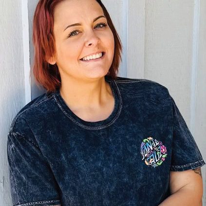 Smiling woman with red hair in a black T-shirt outside.