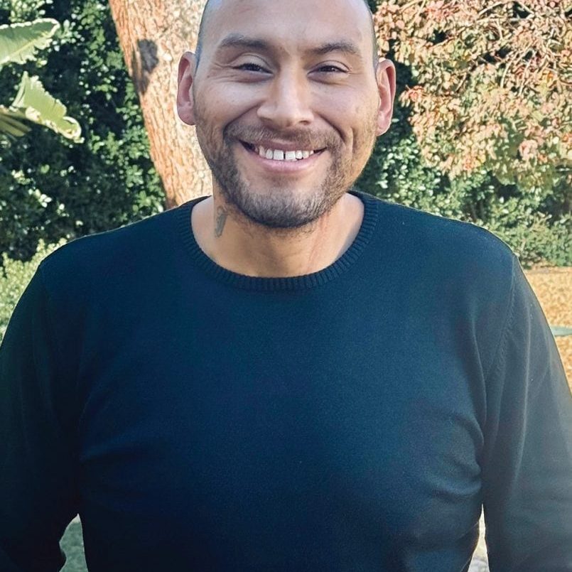 A smiling man at San Fernando Rescue Mission outdoors in sunlight.