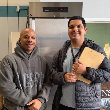 A man and a young adult male standing inside San Fernando Rescue Mission, smiling.