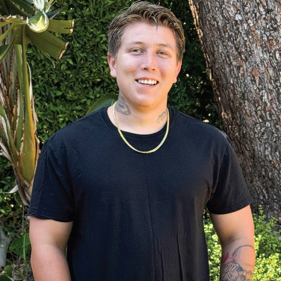 Young man smiling outdoors near trees and greenery at San Fernando Rescue Mission.