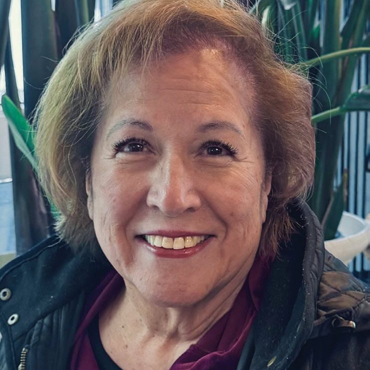 A smiling woman at San Fernando Rescue Mission with greenery in the background.